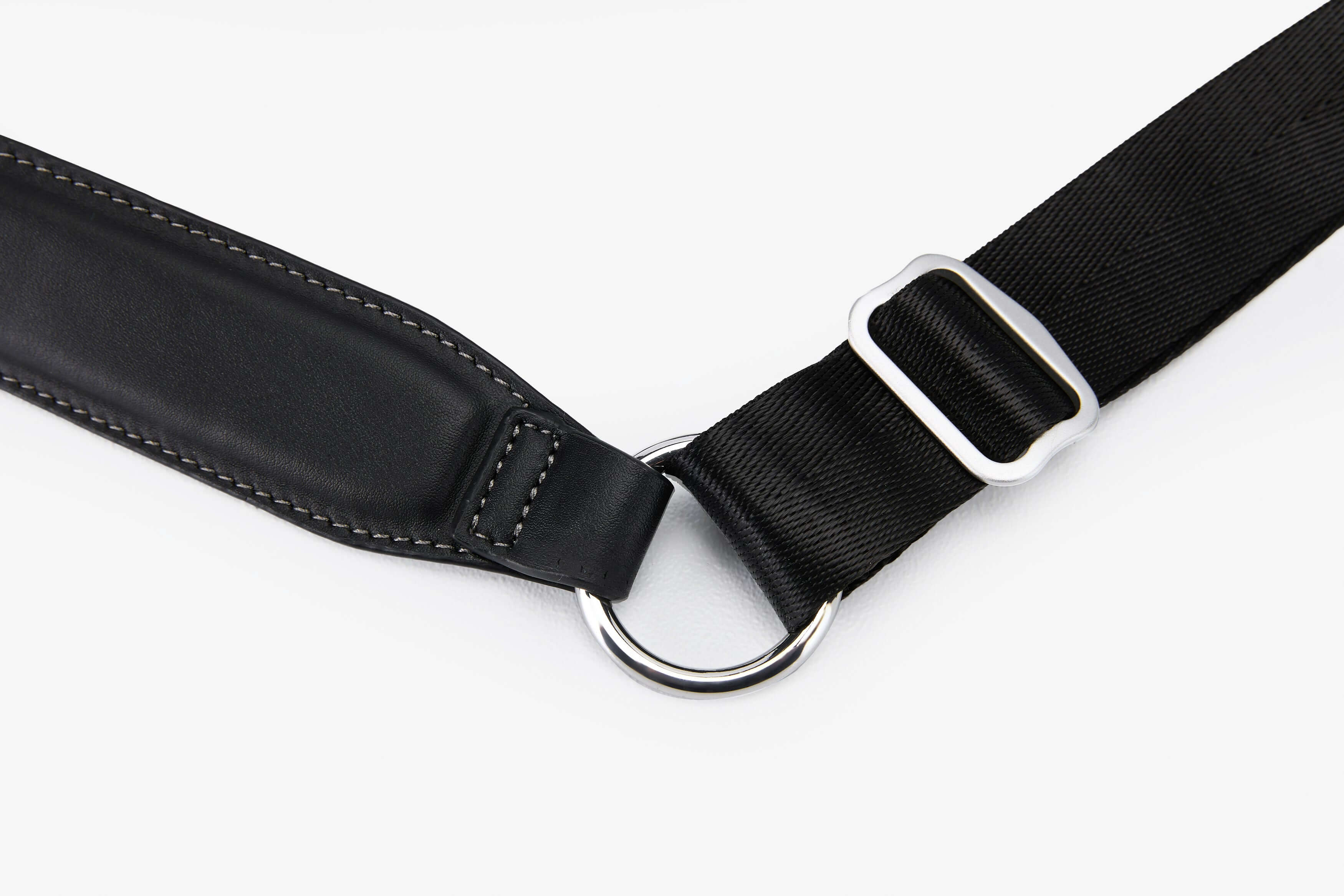 Close-up of a padded crossbody strap with a metallic ring and adjustment buckle, showcasing premium materials.