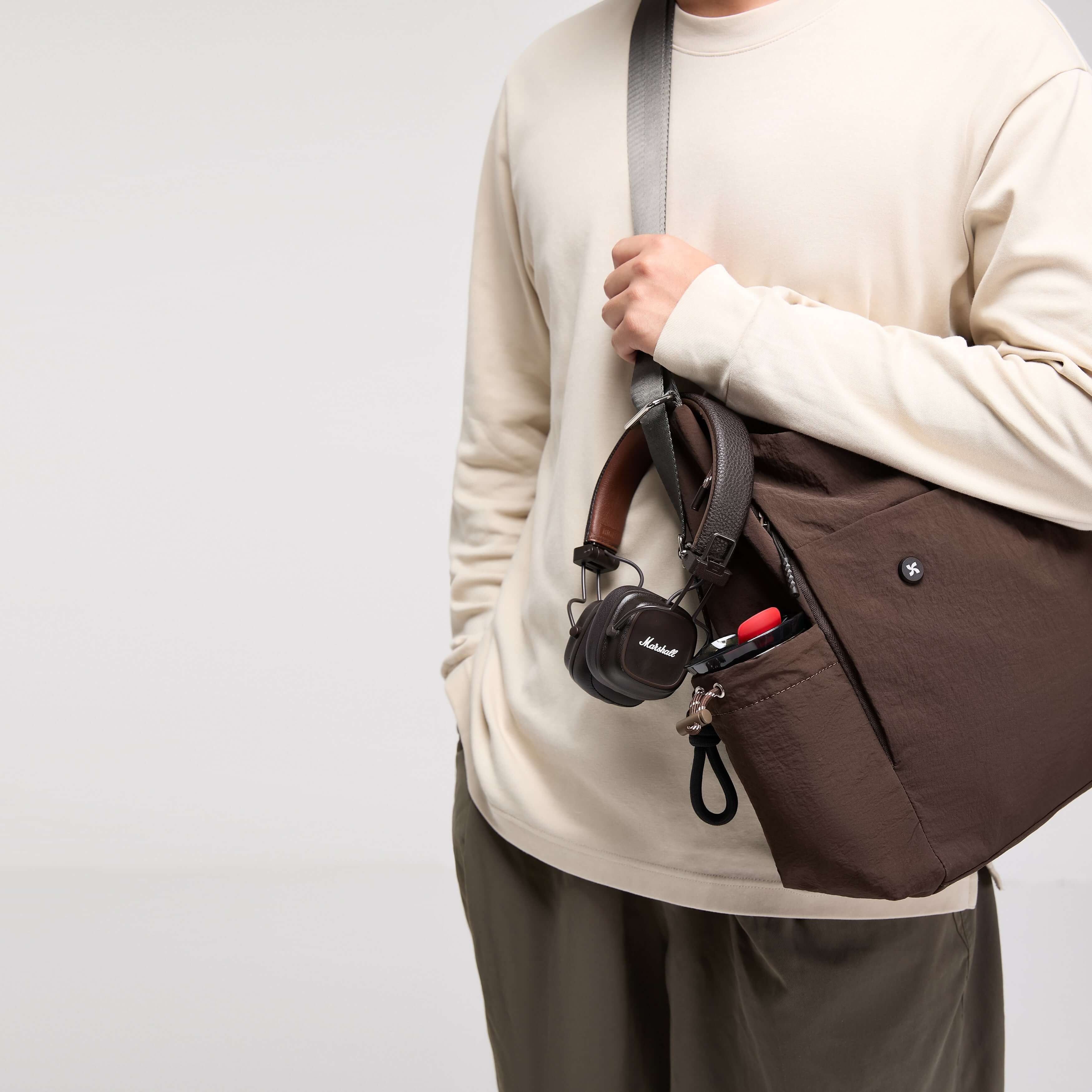 A person wearing a beige long-sleeve shirt carries a brown Air Convert Tote, showcasing the bag's urban style and functionality.