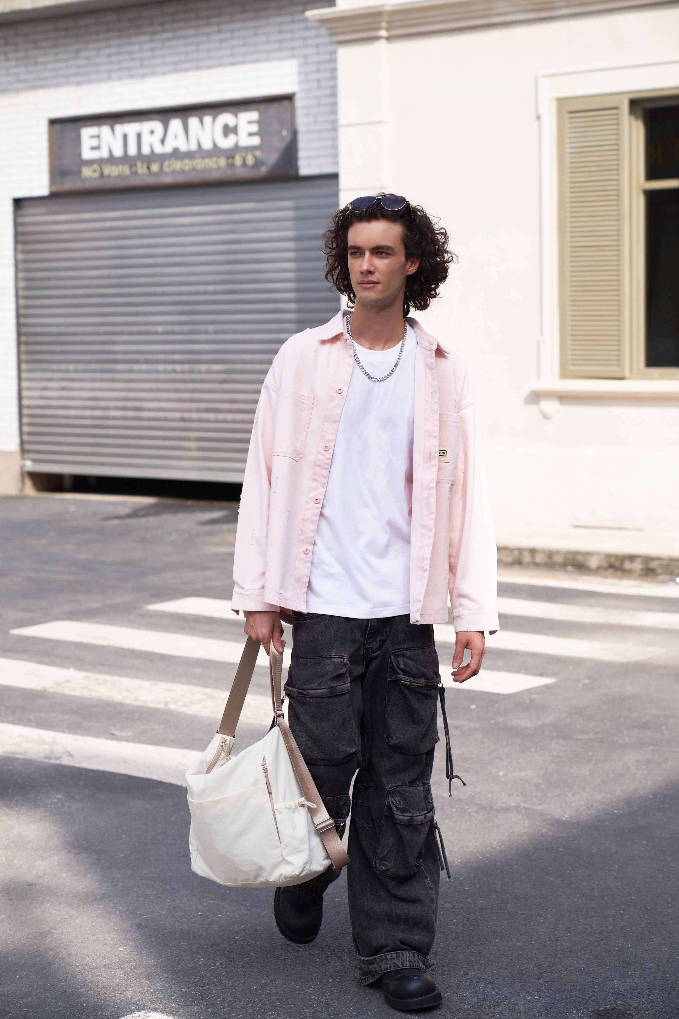 Man walking outdoors holding a white mopak tote bag, wearing a light pink shirt and dark pants.