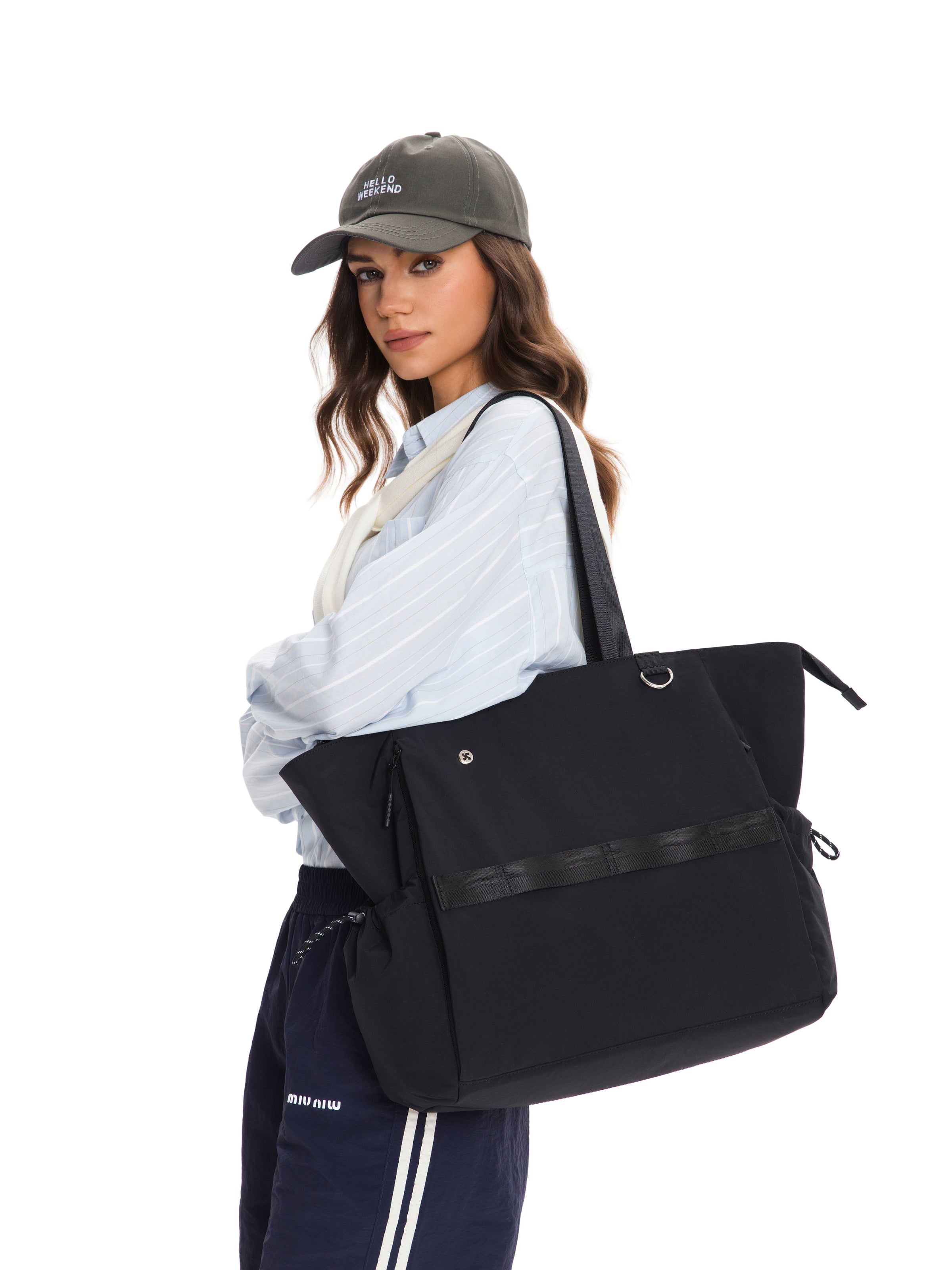 Woman wearing a cap and stylish outfit, holding the Air Daily Tote bag in black.
