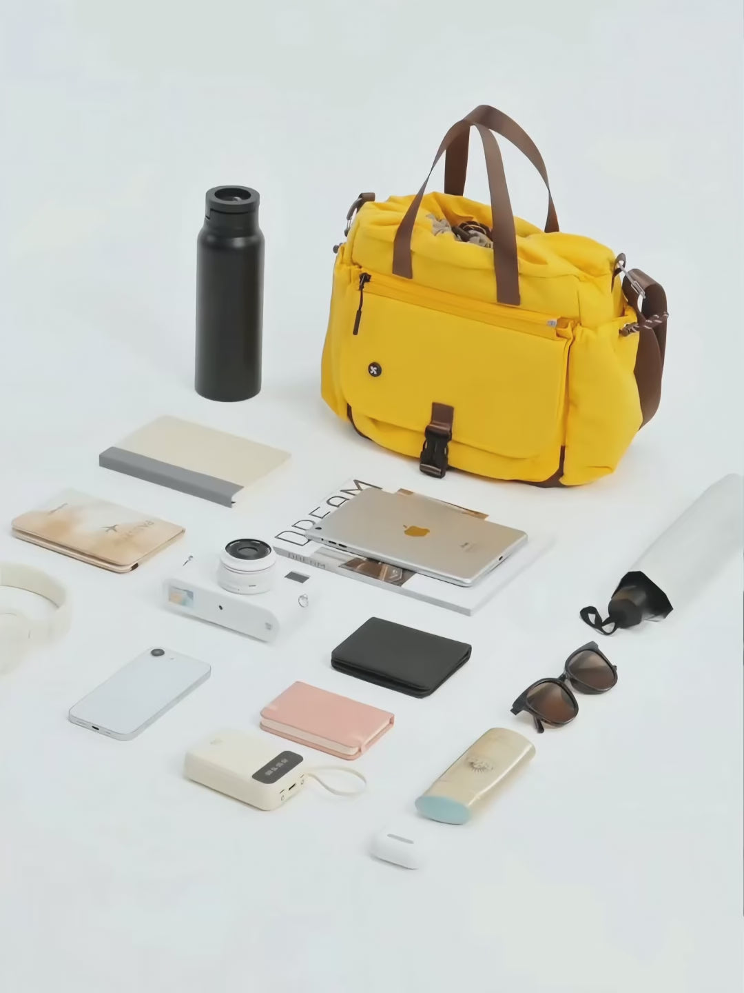 Coast Bucket Bag in yellow surrounded by everyday essentials like a water bottle, laptop, and smartphones.
